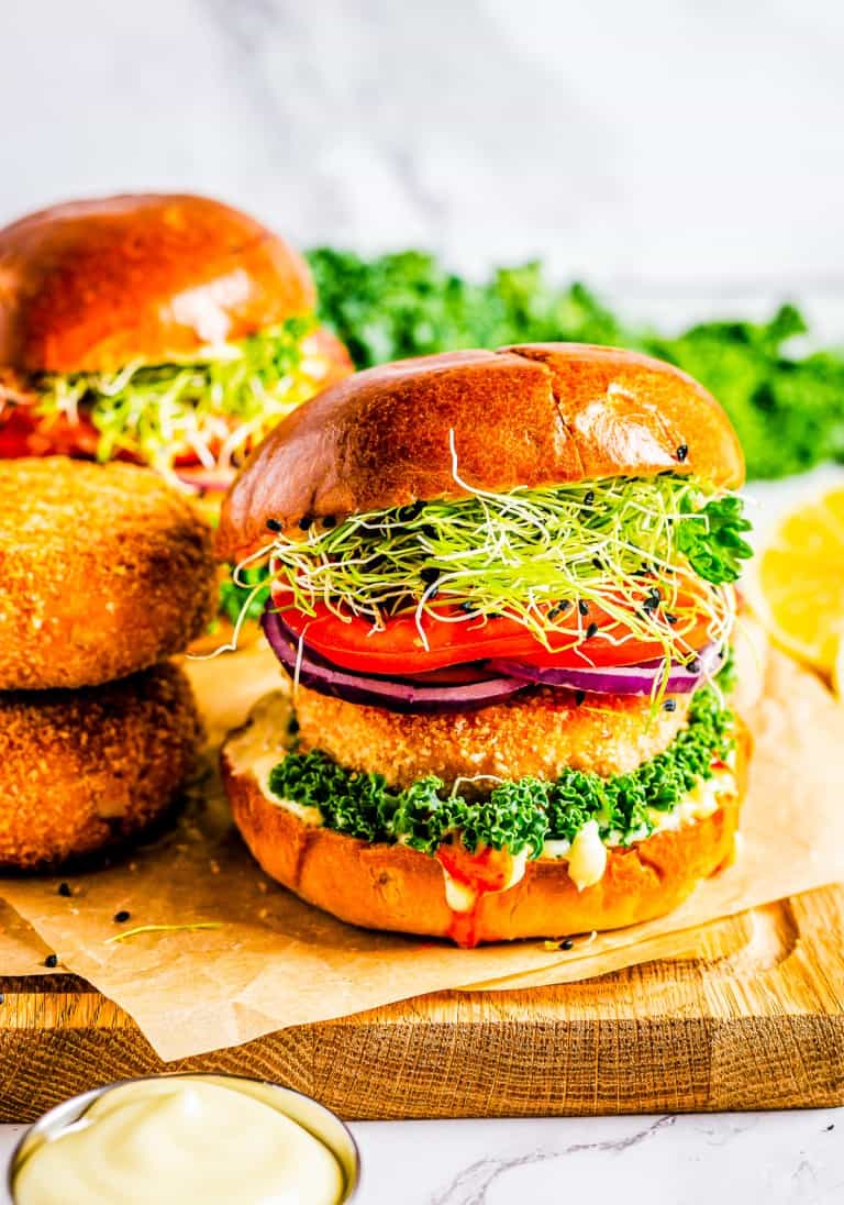 A crispy salmon burger on a brioche bun with lettuce, tomato, and red onion on a wooden board.