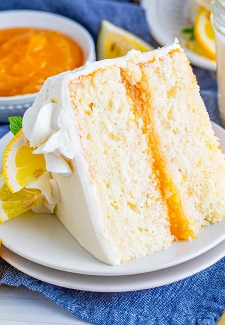 Slice of lemon layer cake on plate with slices of lemon.
