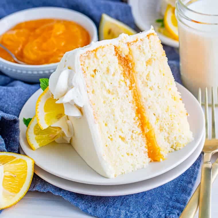 Slice of lemon layer cake on plate with slices of lemon.