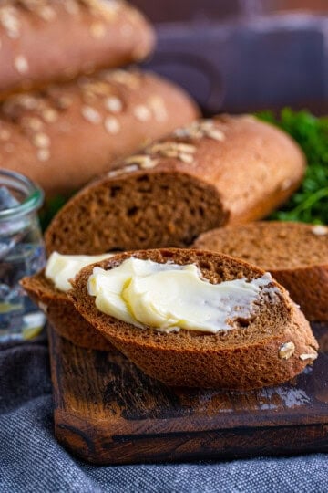 A slice of Cheesecake Factory brown bread spread with butter on a marble surface.