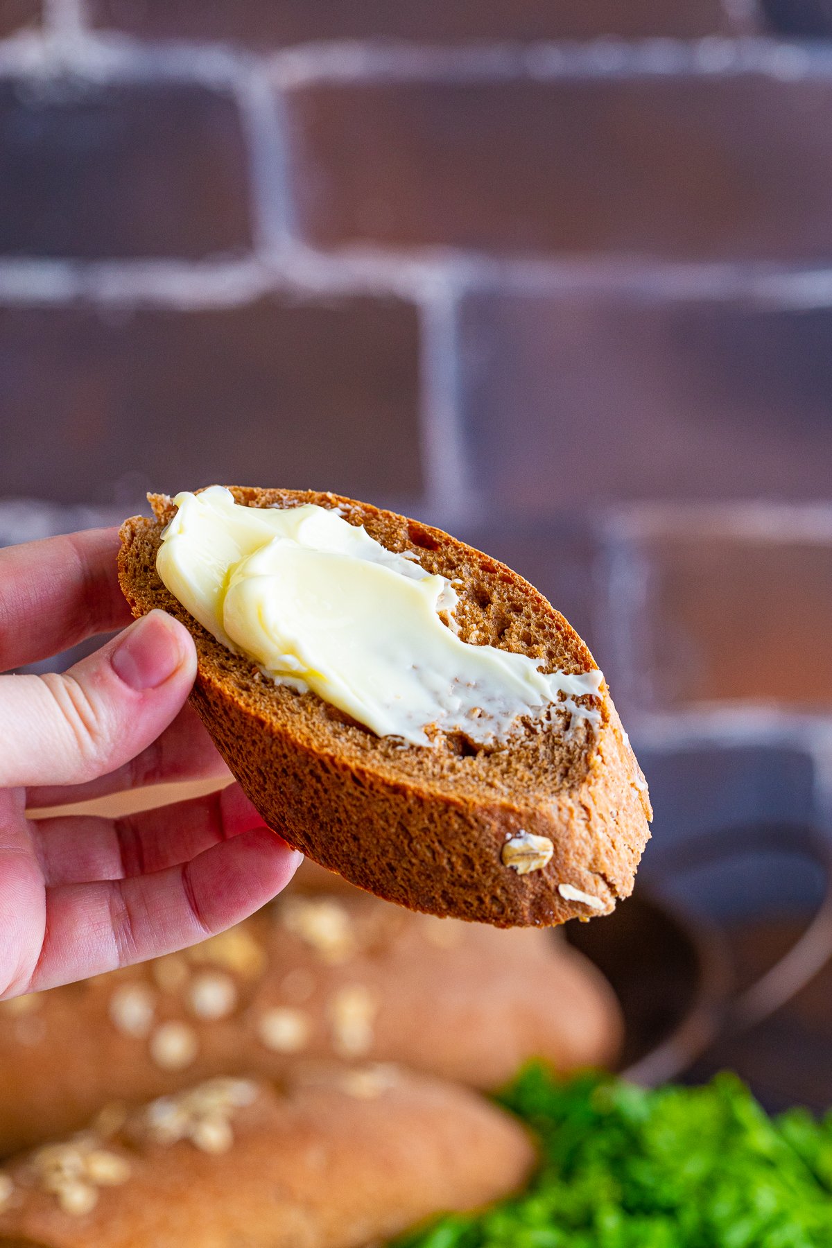 Hand holding up one slice of Brown Bread slathered with butter.