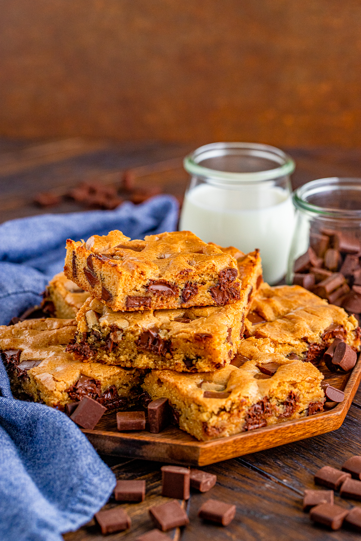 Stacked Chocolate Chunk Blondies on wooden board with milk behind them.