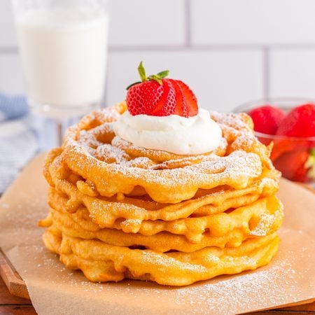 Stacked Funnel Cake Recipe with powdered sugar, whipped cream and strawberries.