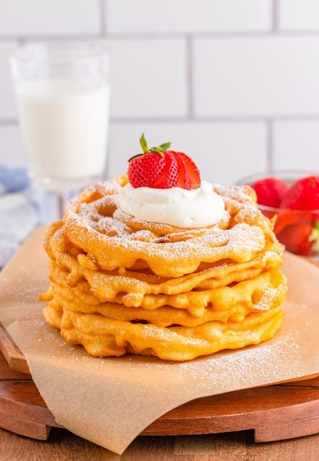 Stacked Funnel Cake Recipe with powdered sugar, whipped cream and strawberries.