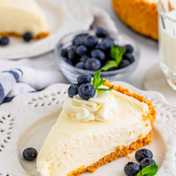 One slice of No Bake Cheesecake on white plate topped with whipped cream, blueberries and mint.