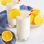 Two glasses of Frosted Lemonade on white board with lemons.