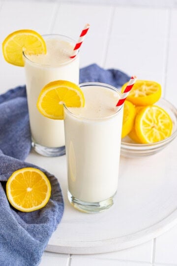 Two glasses of copycat Chick-fil-A frosted lemonade with lemon slices and striped straws.