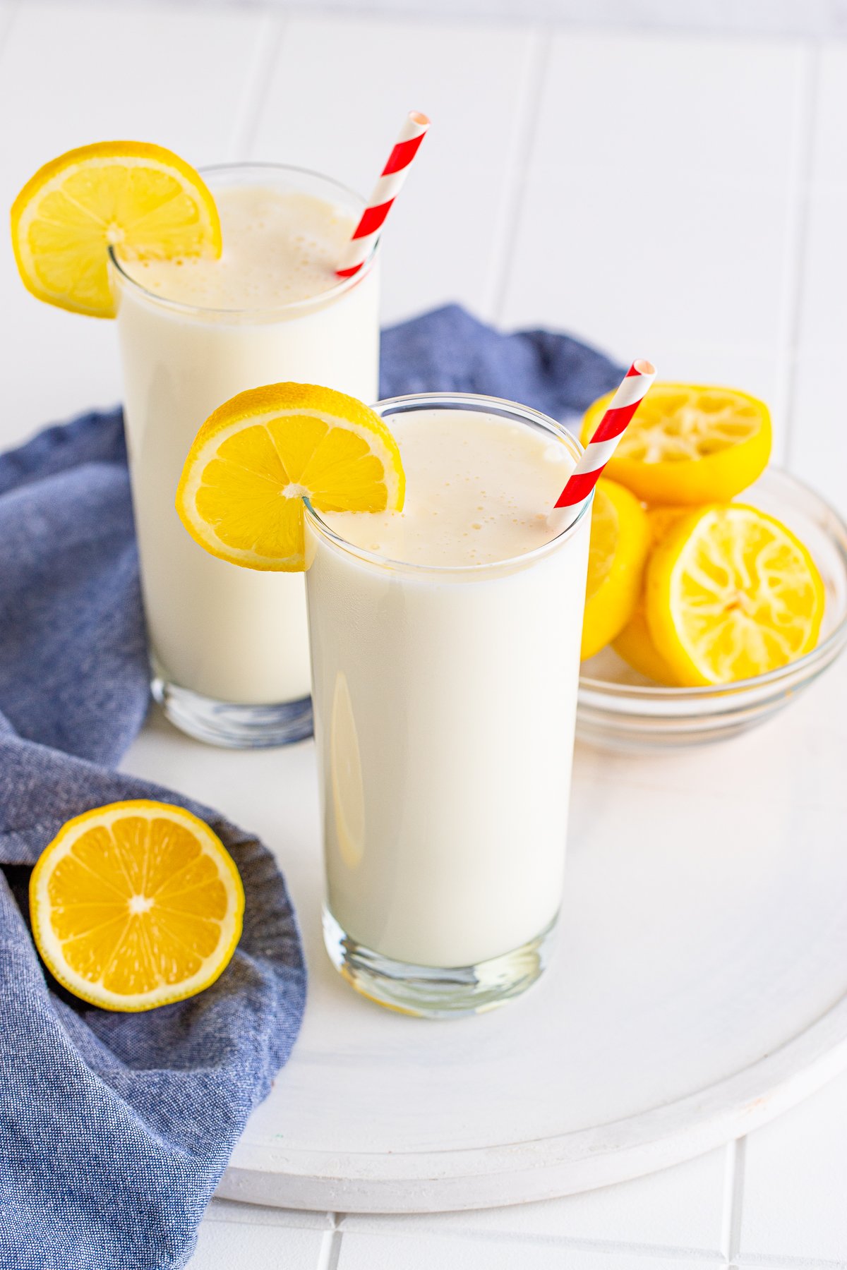 Two glasses of Frosted Lemonade on white board with lemons.