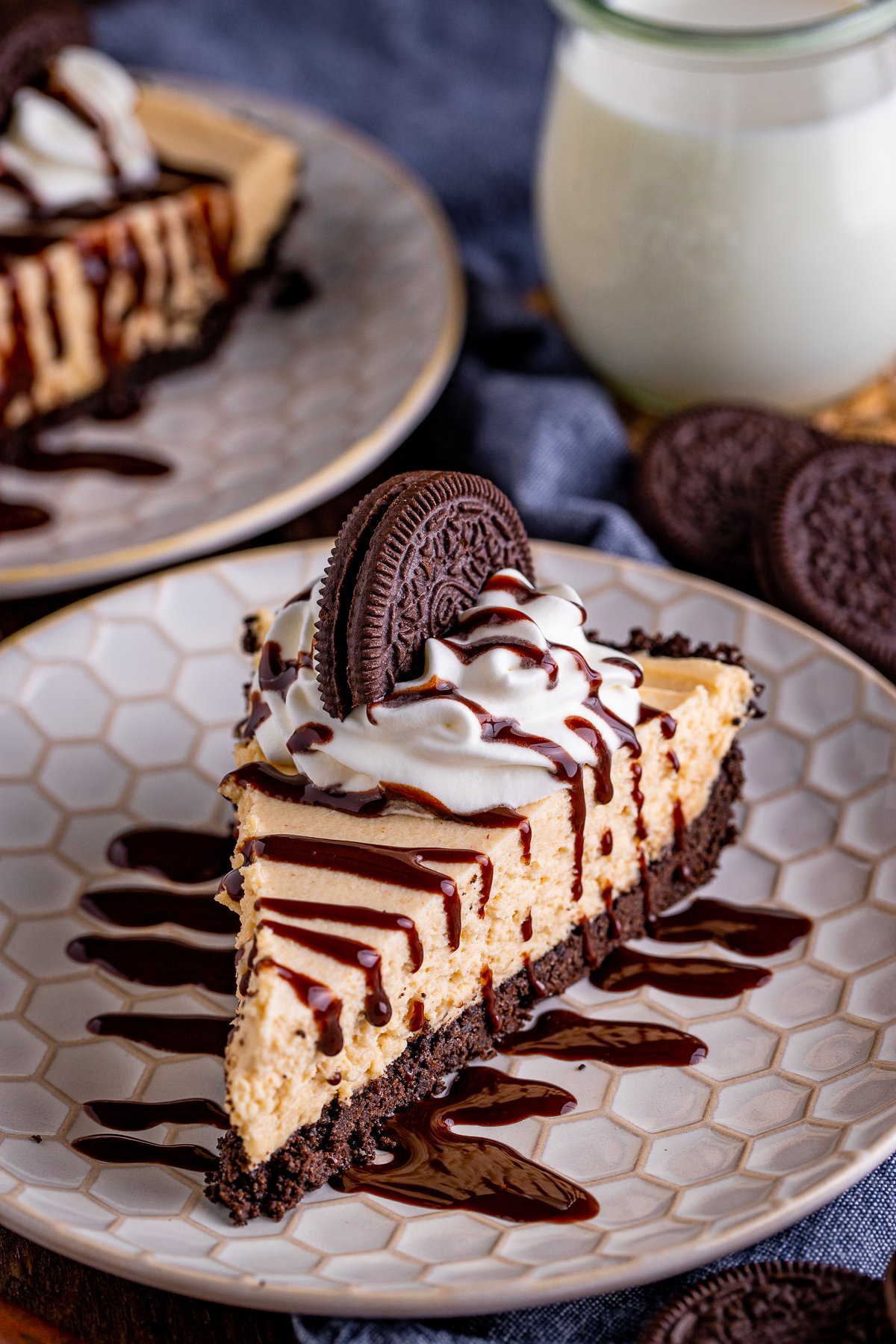 Slice of No Bake Peanut Butter Pie on plate drizzled with chocolate, topped with whipped cream and oreo.