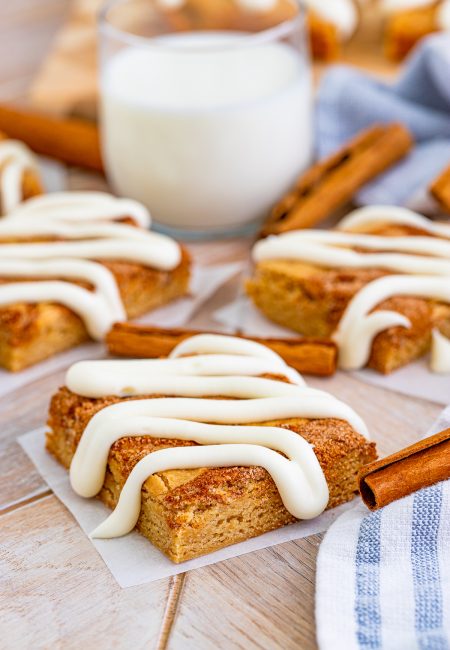 Cinnamon Roll Blondies on parchment paper in front of glass of milk.