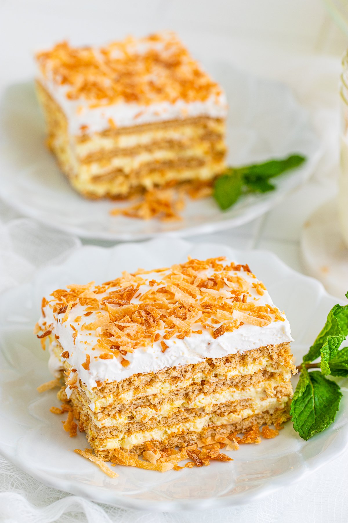 Two slices of Coconut Icebox Cake on plates with mint leaves.