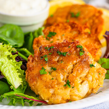 Close up of layered Crab Cake Recipe on plate with salad and dipping sauce.