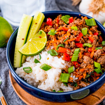 Garished Thai Beef Bowl on wooden plate with water and lime on the sides.