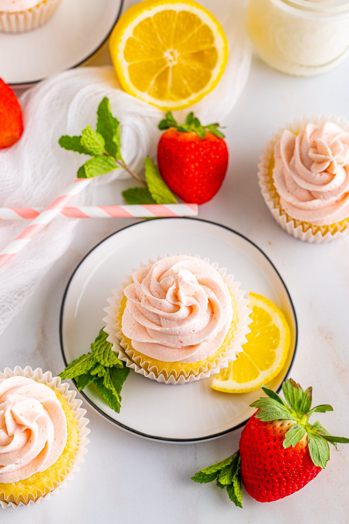 Overhead of Lemon Cupcakes with one on plate with lemons, strawberries and mint.