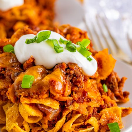 Close up of Frito Chili Pie Casserole on white plate with sour cream and scallions.