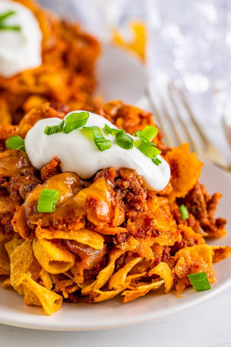Close up of Frito Chili Pie Casserole on white plate with sour cream and scallions.