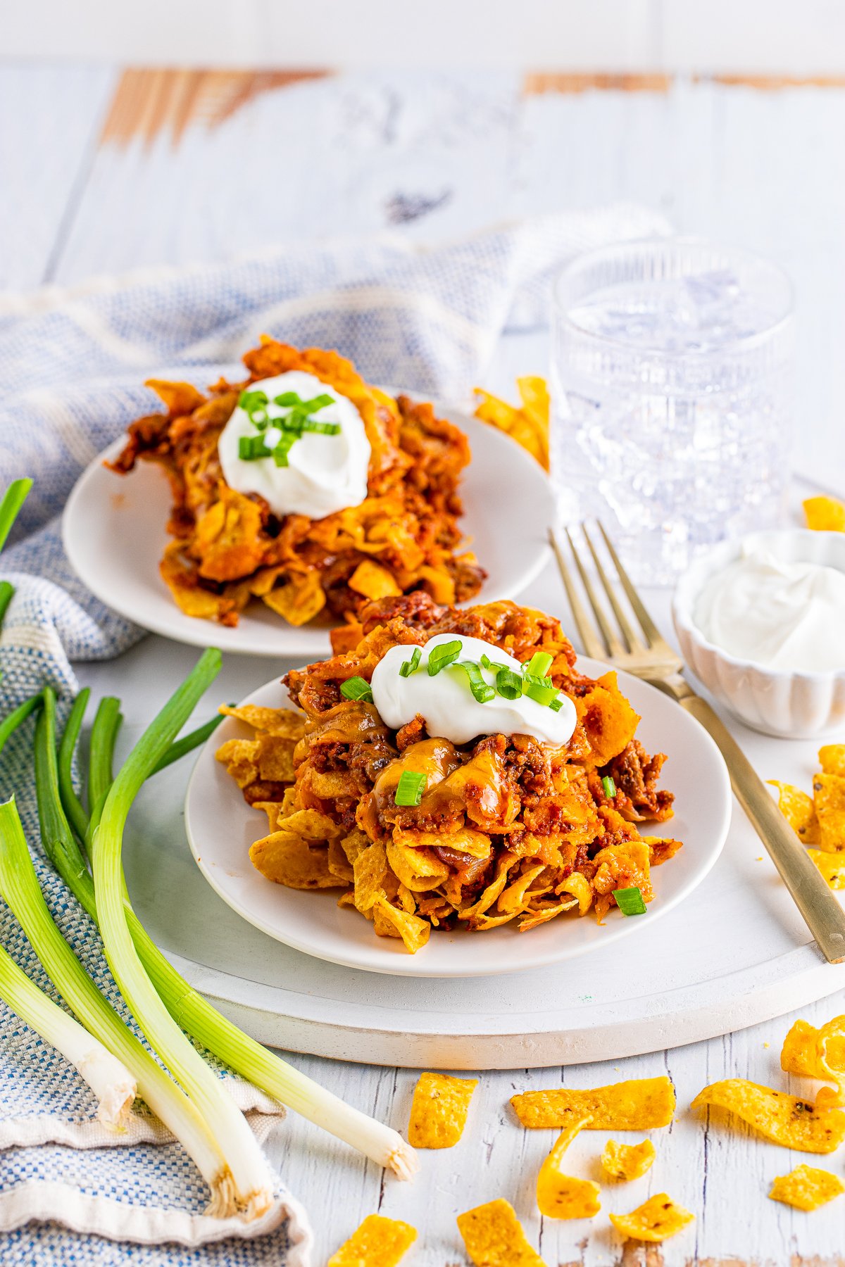 Two plates with Frito Chili Pie Casserole topped with sour cream and scallions.