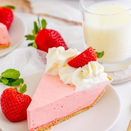 Slice of Strawberry Jello Pie on white plate topped with whipped cream and strawberry.
