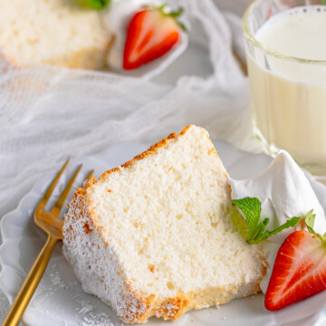 Close up of one slice of the Angel Food Cake Recipe on white plate with whipped cream and berries.