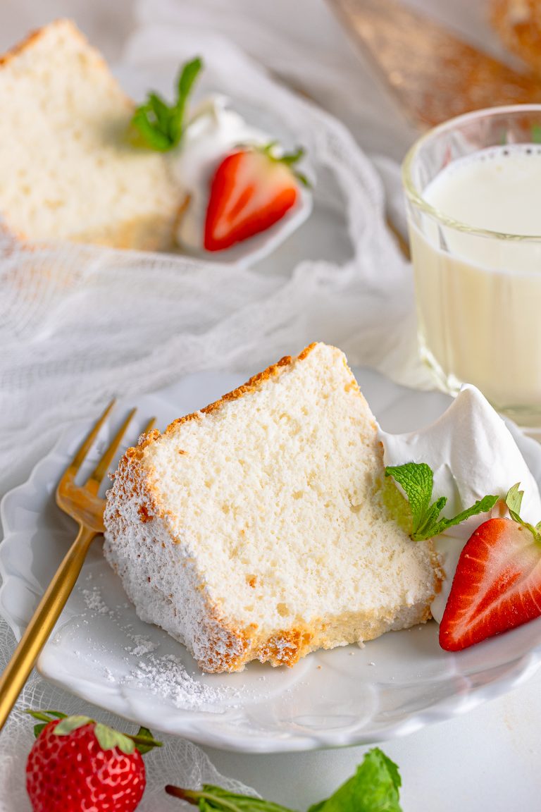 Close up of one slice of the Angel Food Cake Recipe on white plate with whipped cream and berries.