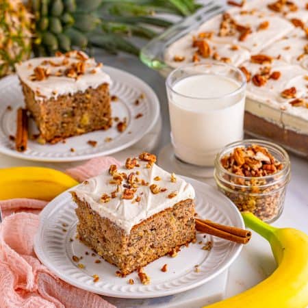 Two slices of Hummingbird Cake on white plate with nuts on top and milk beside them.