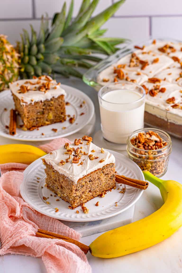Two slices of Hummingbird Cake on white plate with nuts on top and milk beside them.