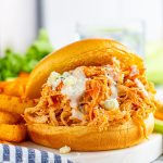 Close up of one finished Slow Cooker Buffalo Chicken Sandwiches next to fries.