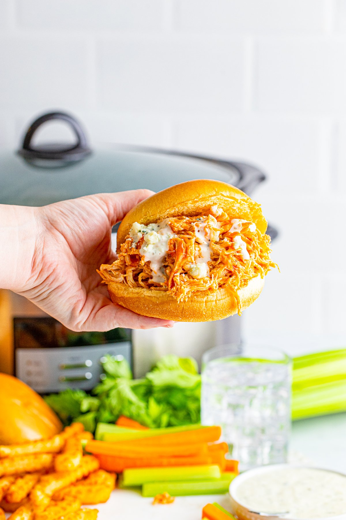 Hand holding up one of the Slow Cooker Buffalo Chicken Sandwiches showing the toppings.
