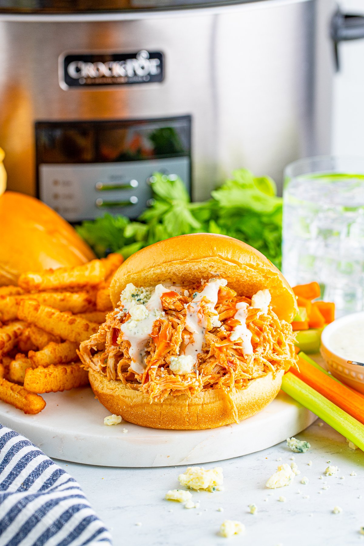 Slow Cooker Buffalo Chicken Sandwich on white platter with dressing served with fries.