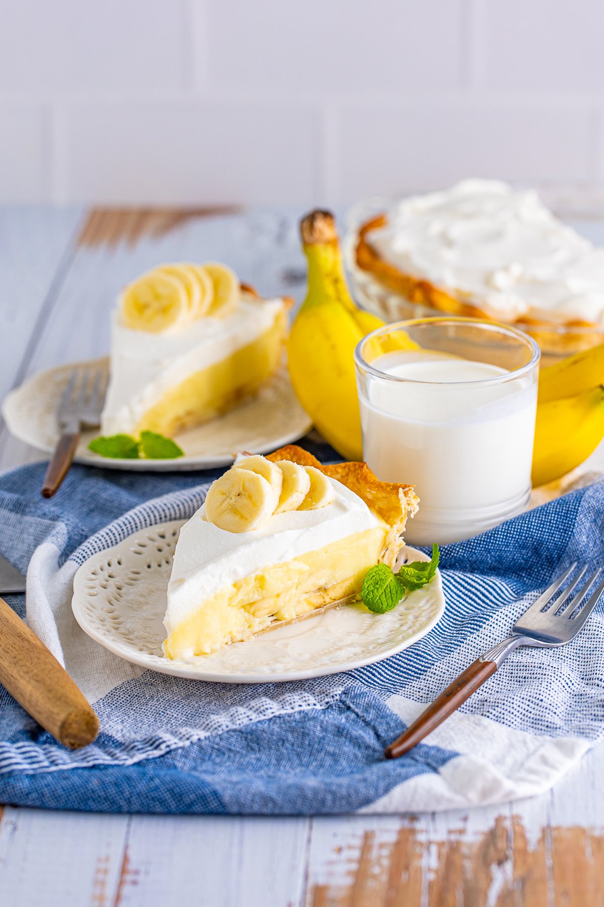 Two slices of Banana Cream Pie on white plates topped with banana slices.