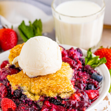 Berry Cobbler on plate side view topped with ice cream with milk in background.