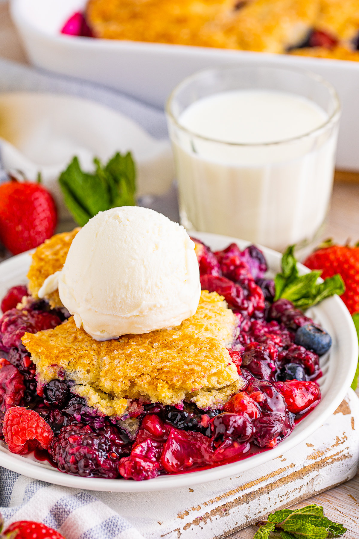 Berry Cobbler on plate side view topped with ice cream with milk in background.