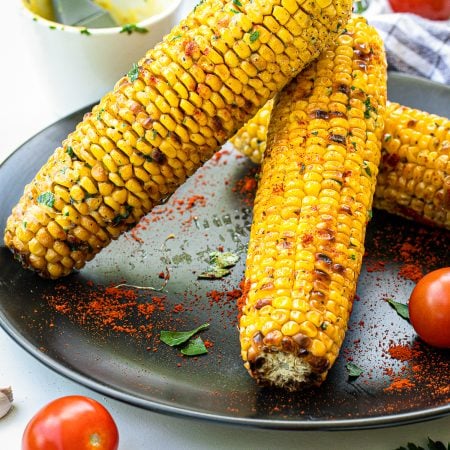 Close up of stacked Grilled Corn on black plate.