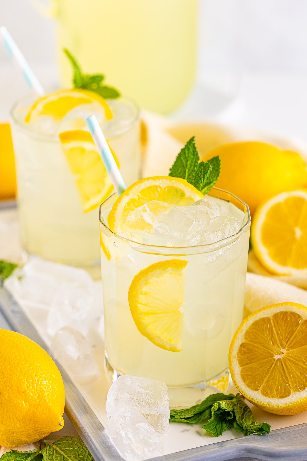Two glasses of the Lemonade REcipe no metal tray with ice and lemons.