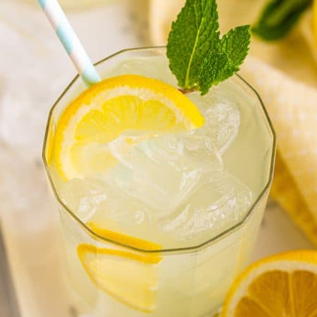 A close-up glass of homemade lemonade over ice with a fresh lemon slice and mint.