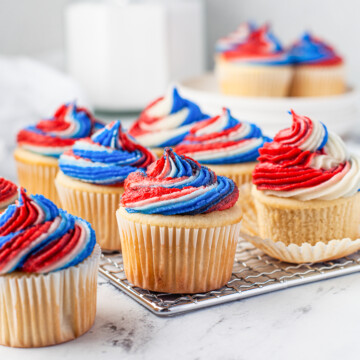 Lined up Patriotic Cupcakes on wire rack and marble board with milk in background.