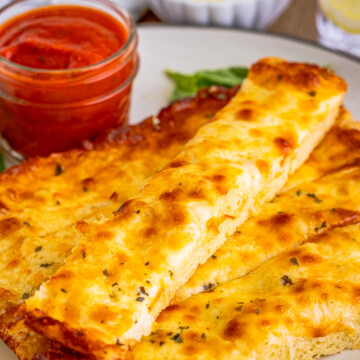 Side view of stacked Pizza Hut Cheese sticks on white plate with marinara sauce.