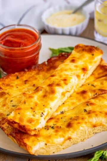 Copycat Pizza Hut cheese sticks on a plate with a cup of marinara sauce for dipping.