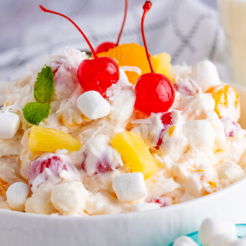 Close up of Ambrosia Salad Recipe in serving bowl topped with cherries and mint.