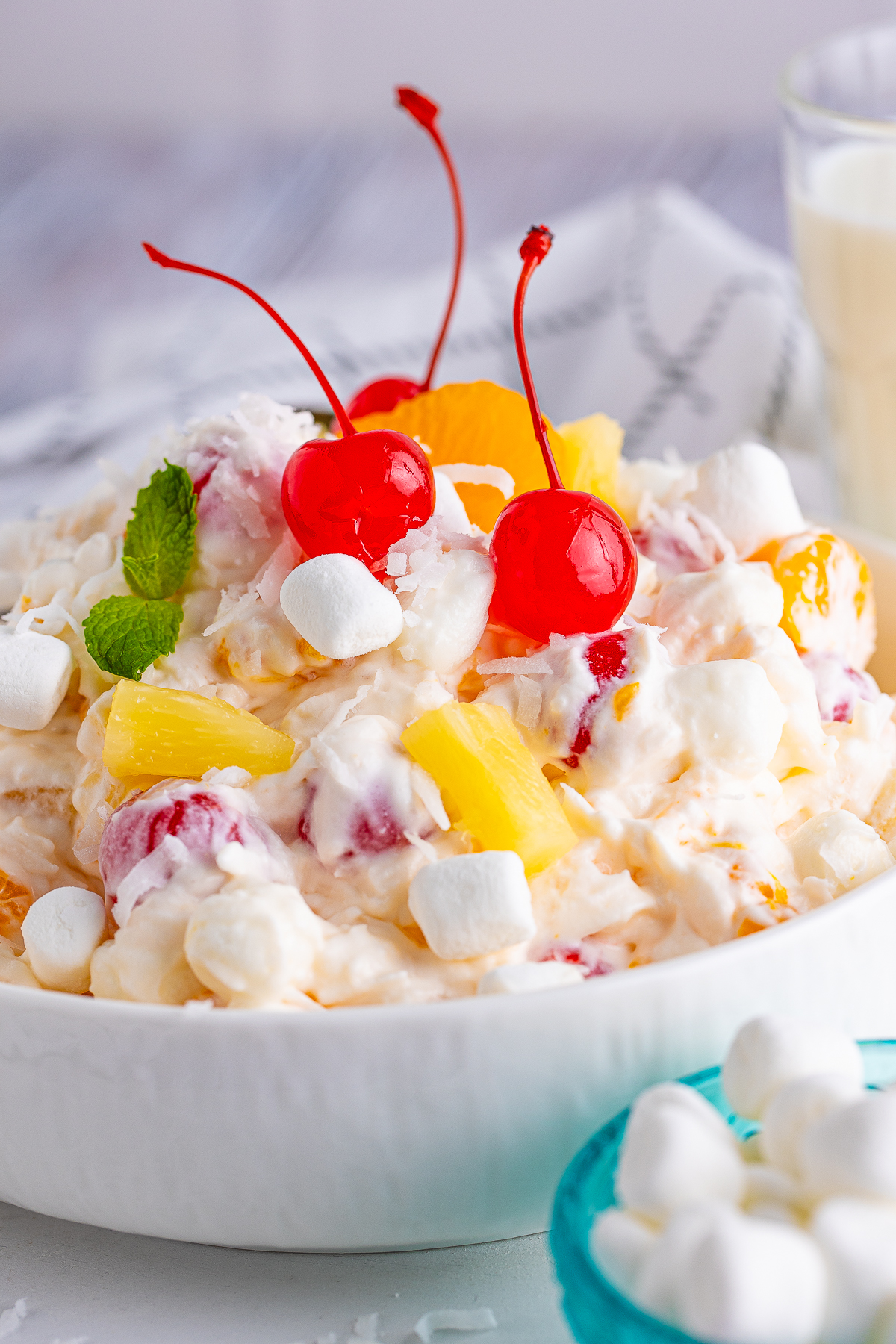 Close up of Ambrosia Salad Recipe in serving bowl topped with cherries and mint.