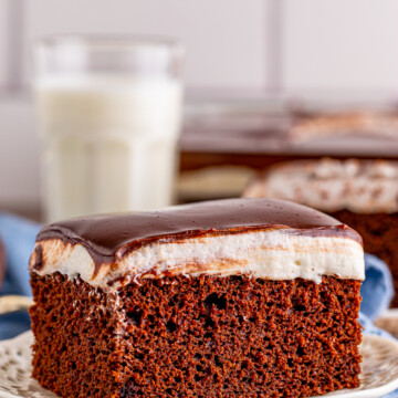 Close up of one slice of Ding Dong Cake on white plate showing layers with milk in background.