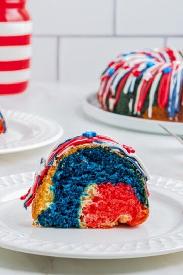 Slice of red, white, and blue 4th of July Cake on a white plate with the whole cake behind it.