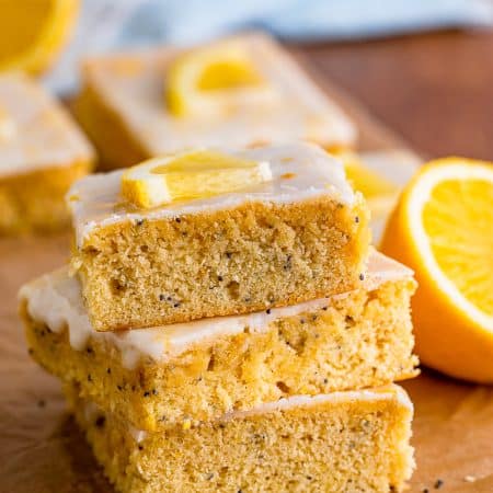 A stack of lemon poppyseed bars showing the poppy speckled crumb and lemon glaze.