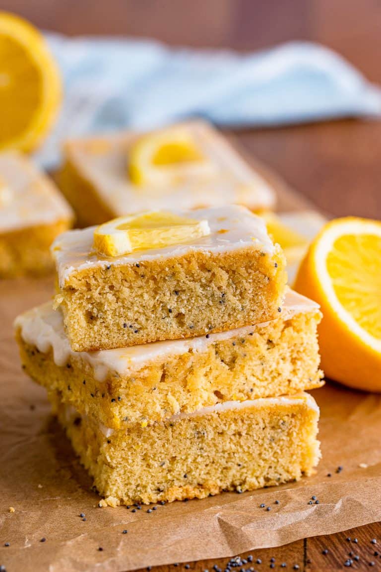 A stack of lemon poppyseed bars showing the poppy speckled crumb and lemon glaze.