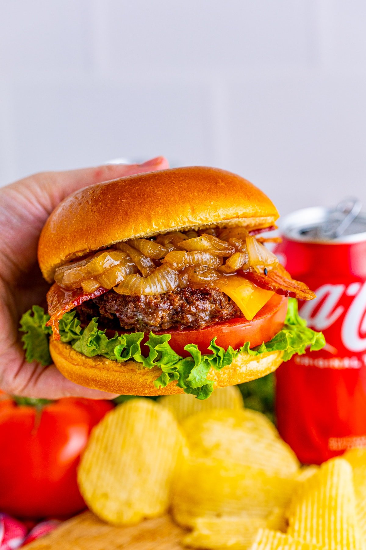 Hand holding up one of the finished Bacon Cheeseburgers with Coca-Cola Onions showing layers.