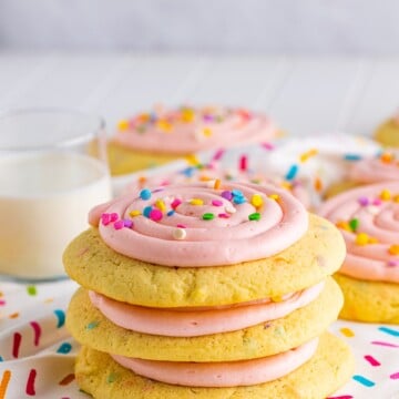 Three stacked Confetti Cake Cookies on linen with glass of milk behind it.