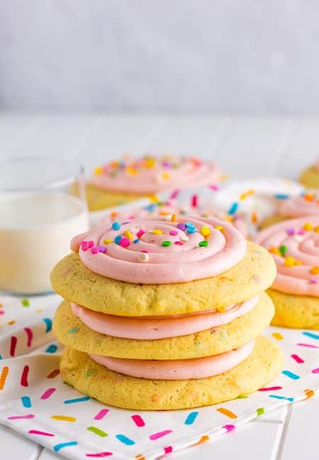 Three stacked Confetti Cake Cookies on linen with glass of milk behind it.