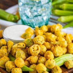 Fried Okra Recipe on wooden plate with dipping sauce and water in background.