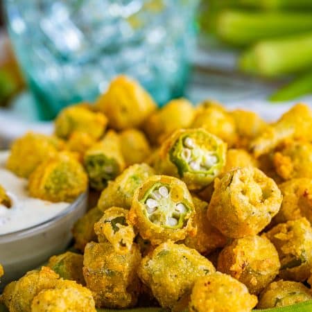 A heaping pile of golden crispy fried okra with a bowl of ranch dressing for dipping
