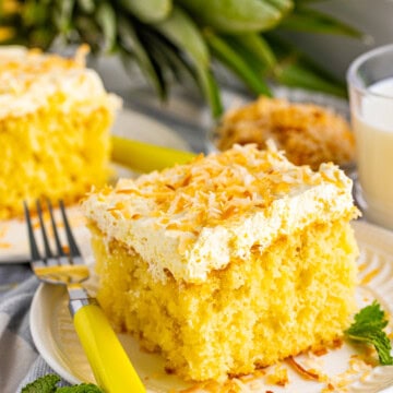 Slice of Pina Colada Cake on white plate topped with toasted coconut.